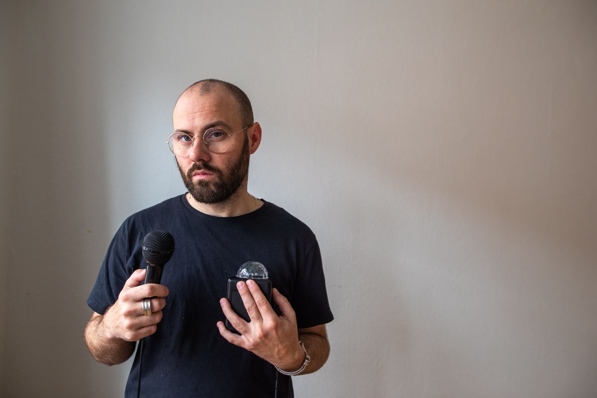 Marc Facchini holding a microphone against a pale wall
