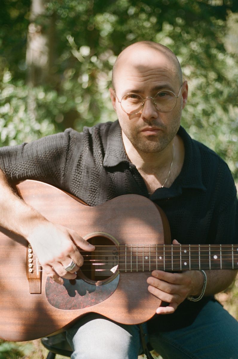 Marc Facchini with acoustic guitar among green trees